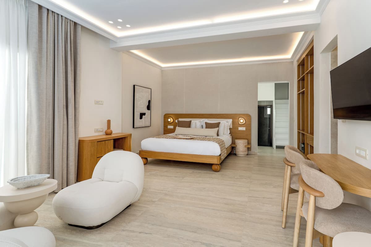 A modern hotel room with a large bed, a wooden desk, a chair, a small table, and a TV.