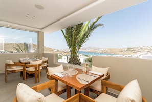 A dining area with a wooden table and chairs, a large window with a view of a coastal landscape.