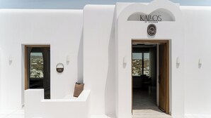 A white building with a sign reading 'KALOS OF MYKONOS,' a gym entrance, and a doorway leading inside. - Kallos of Mykonos (Mykonos)