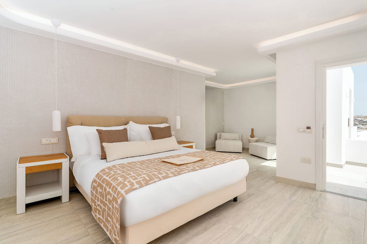A modern hotel room with a large bed, bedside tables, a nightstand, a sofa, and a view of the city.
