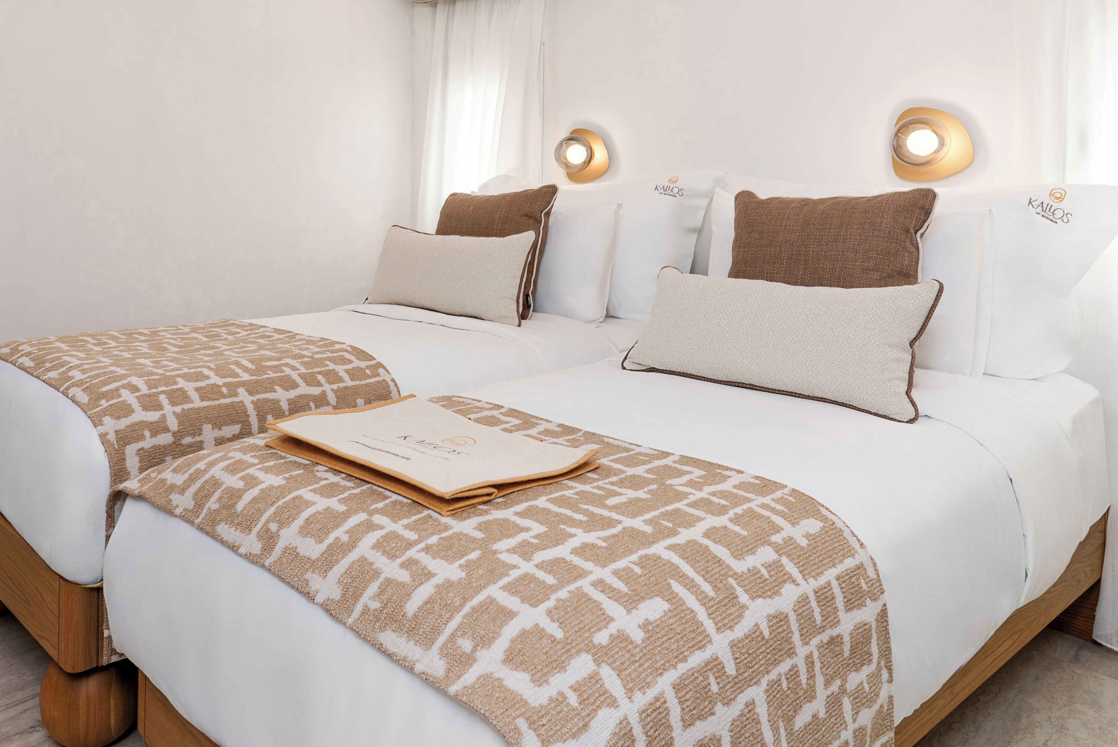 A double bed with a patterned throw, two pillows, a bedside table, and wall-mounted lighting.