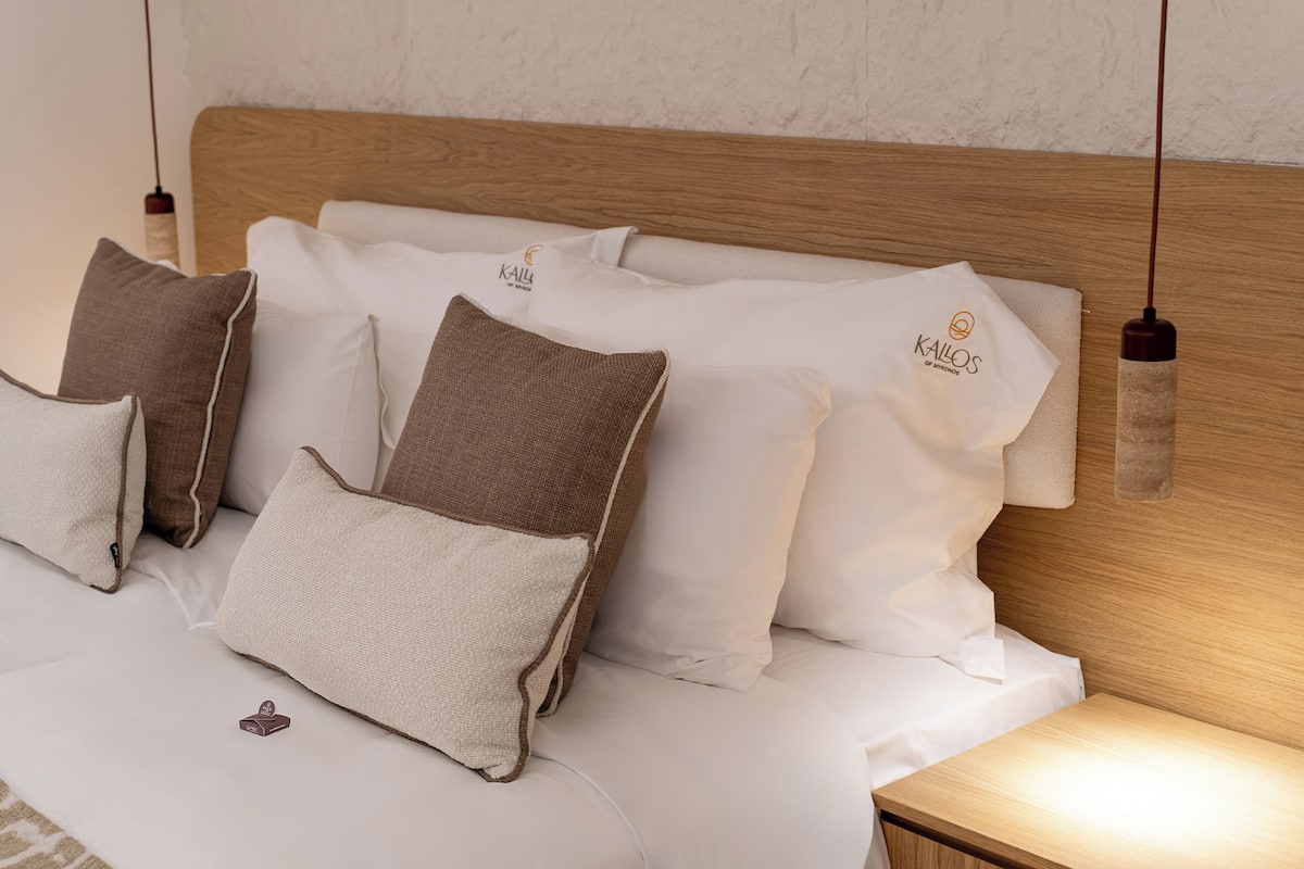 A neatly made bed with white and brown pillows, a wooden headboard, and a small nightstand with a lamp.