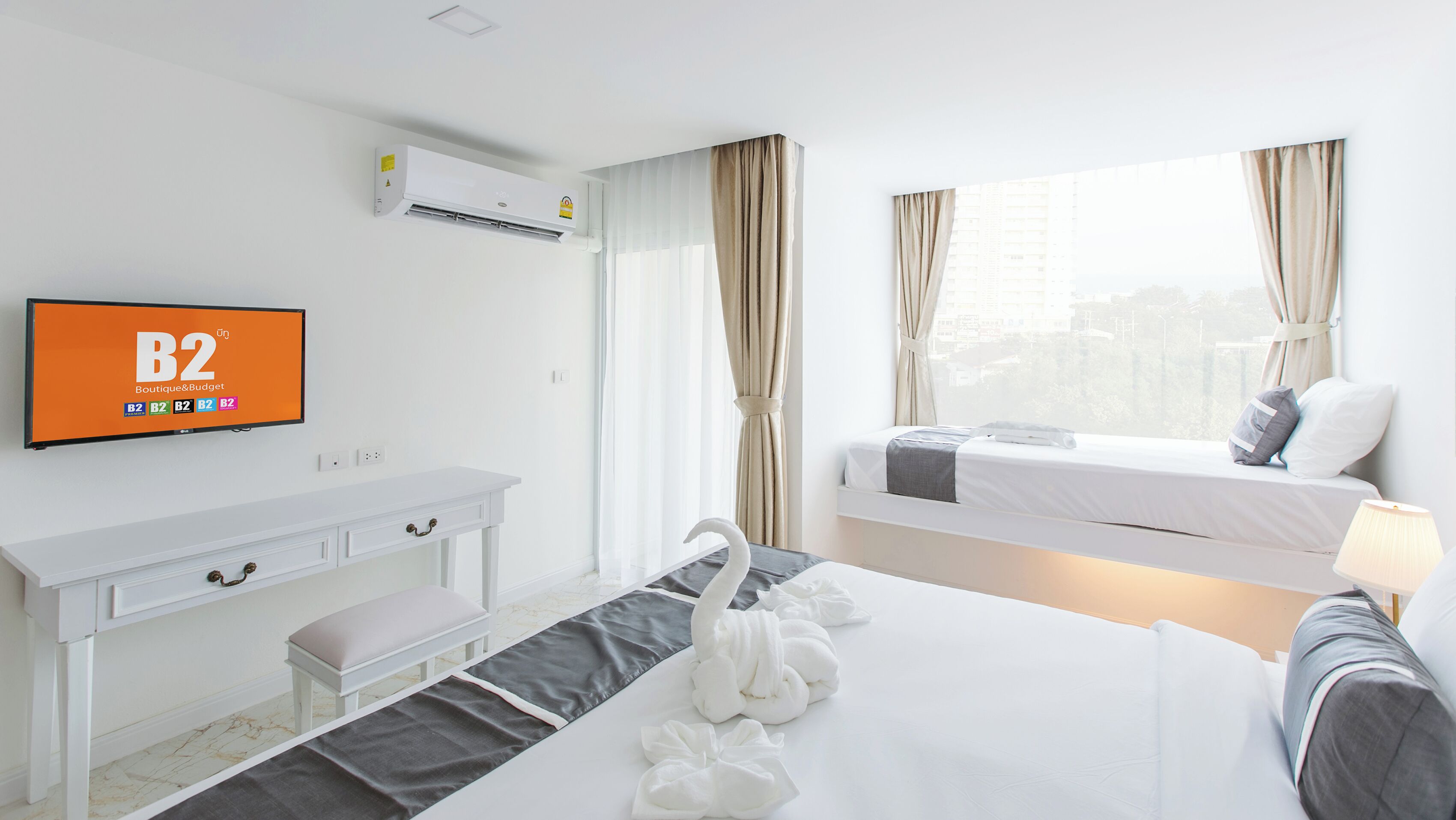 A hotel room with a bed, bedside table, TV, air conditioning unit, and a window with curtains.