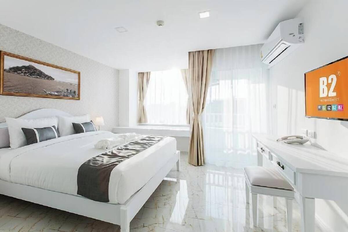 Una habitación de hotel moderna con cama, escritorio, televisión y ventana con cortinas.
