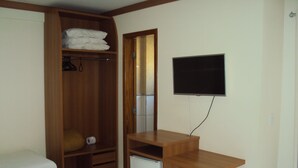 A bedroom with a wooden wardrobe, a bed, a small desk, and a TV mounted on the wall. - Apartamento Grand Dolphin - Férias em Caldas Novas (Caldas Novas)