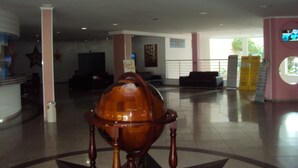 A lobby with a large wooden globe, a reception desk, and a seating area with a railing. - Apartamento Grand Dolphin - Férias em Caldas Novas (Caldas Novas)