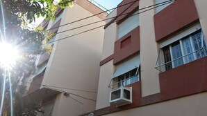 A building with multiple windows, some with shutters, and a visible air conditioning unit. - Apartamento Atalaia (Porto Alegre)