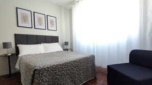 A hotel room with a bed, two bedside tables, a chair, and three framed leaf artworks on the wall. - Apartamento Atalaia (Porto Alegre)