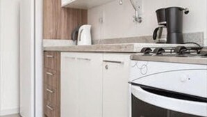 A modern kitchen with white cabinets, a built-in oven, and a coffee maker. - Apartamento Atalaia (Porto Alegre)