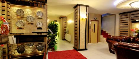A hotel lobby with a red carpet, wooden decor, clocks indicating different cities, a staircase, and leather sofas.
