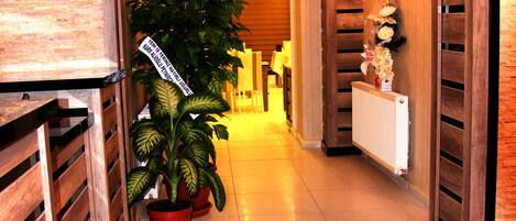 Un pasillo con paneles de madera, plantas en macetas, alfombra roja y un letrero que indica un salón.