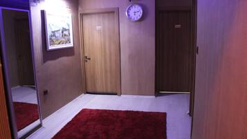 A hallway with a red carpet, wooden doors, a clock, and a framed picture on the wall.