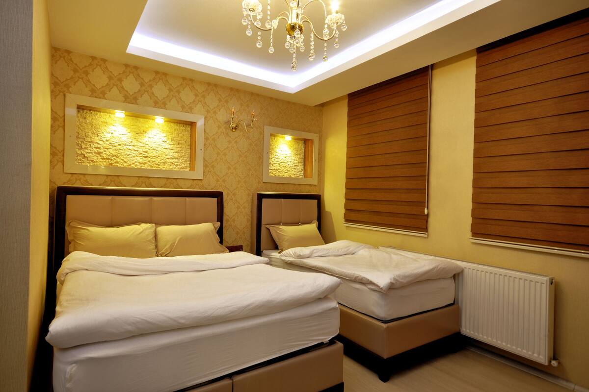 A hotel room with two beds, a chandelier, and a window with blinds.