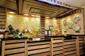 A reception area with wooden slatted counters, a textured stone wall, and multiple clocks on the wall. - Kars Konak Hotel (Kars)