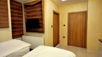Un dormitorio con dos camas, un armario de madera, un televisor montado en la pared y una puerta.