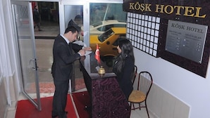 A hotel reception area with a red carpet, a reception desk, and a sign displaying room rates. - Kosk Hotel (Elazig)