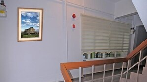 A staircase with a wooden handrail and white balusters, leading to a landing with a closed window and a framed picture on the wall. - Kosk Hotel (Elazig)