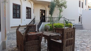 An outdoor seating area with wooden furniture and a stone floor, leading to a staircase and a building entrance. - El Nakhil Hotel (Luxor)