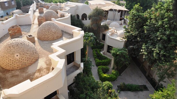 A courtyard with multiple buildings, some with domed roofs and others with flat roofs. There are trees and greenery around the courtyard. - El Nakhil Hotel (Luxor)