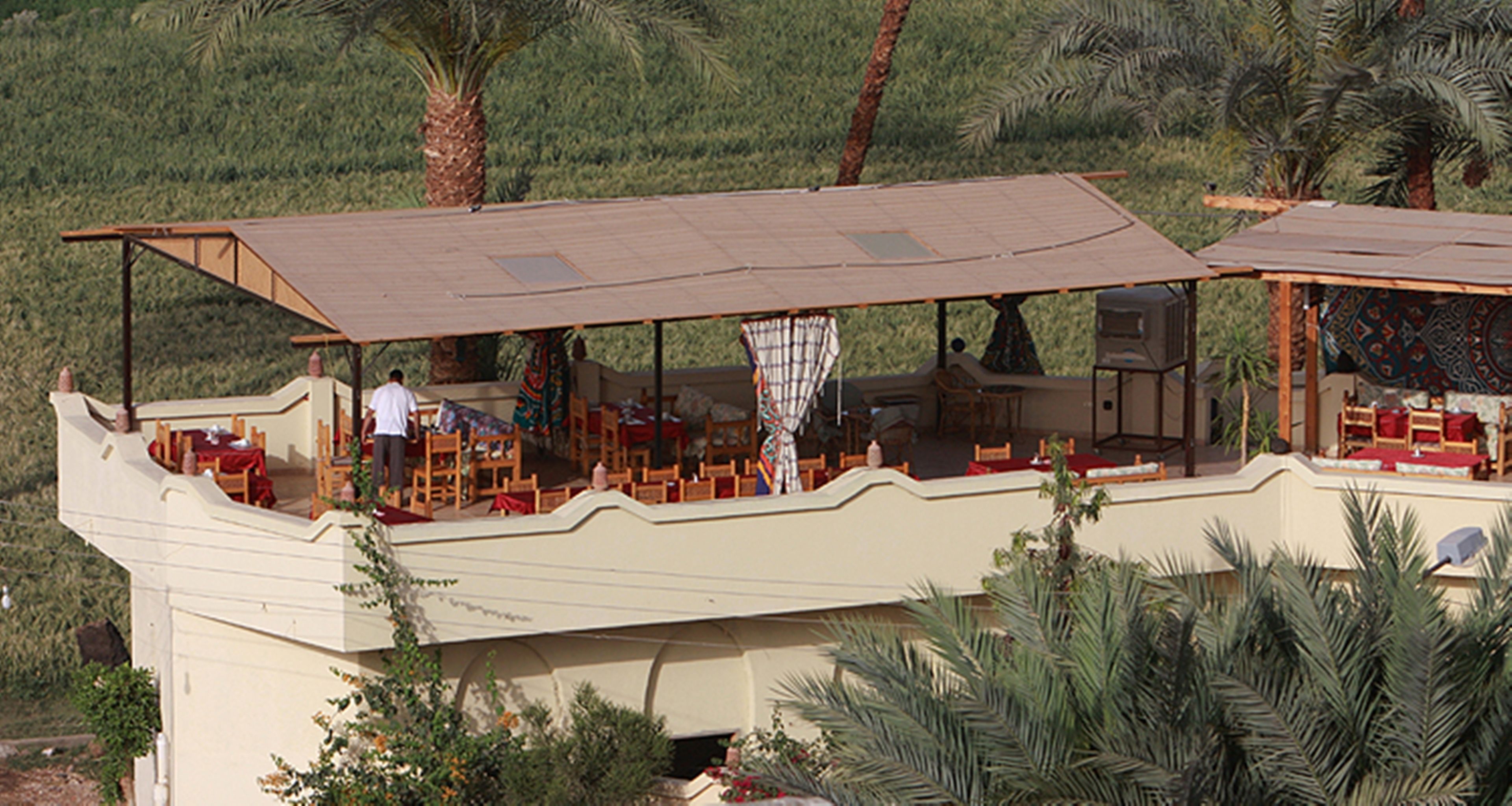 A restaurant with outdoor seating on a raised deck, surrounded by palm trees.