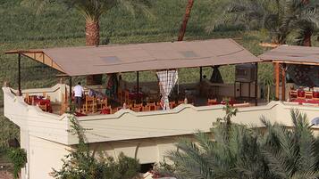 A restaurant with outdoor seating on a raised deck, surrounded by palm trees.