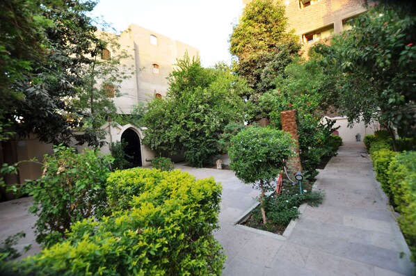 Un patio exterior con un sendero de piedra, rodeado de abundante vegetación y un pequeño arco.
