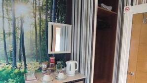 Een kamer met een muurschildering van een bos, een houten kast met lades, een spiegel en een deur met een rookverbodsgeeltje.