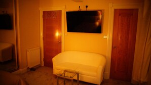 Een kamer met een witte bank, een klein glazen tafeltje en een flatscreen televisie aan de muur.