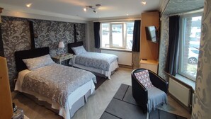 Een hotelkamer met twee bedden, een televisie, een stoel, een raam met uitzicht en een plafondlamp.