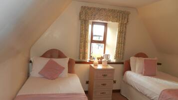 A bedroom with two single beds, a nightstand, a window with curtains, and a lamp.