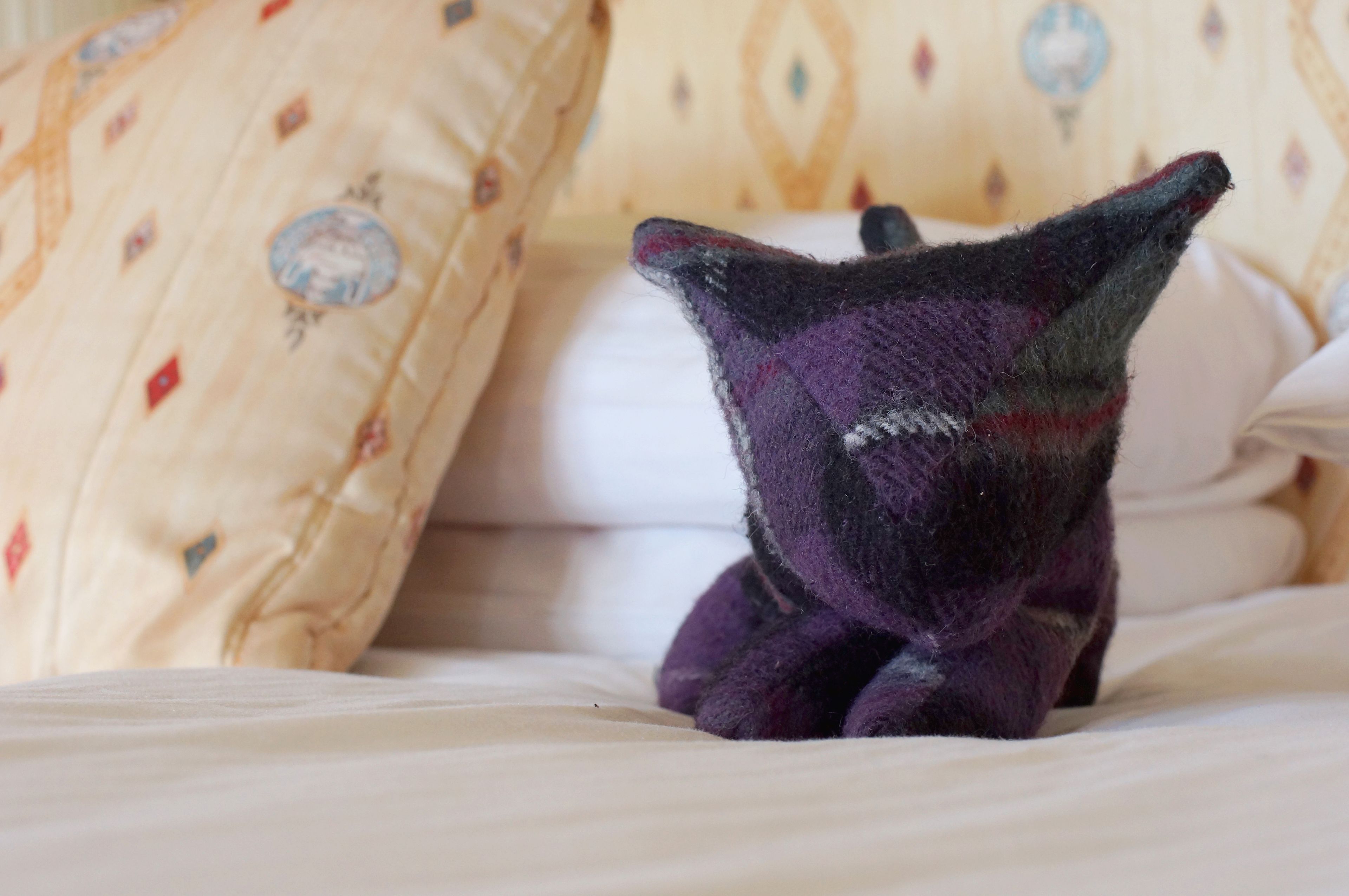 A plush toy on a bed with patterned pillows.