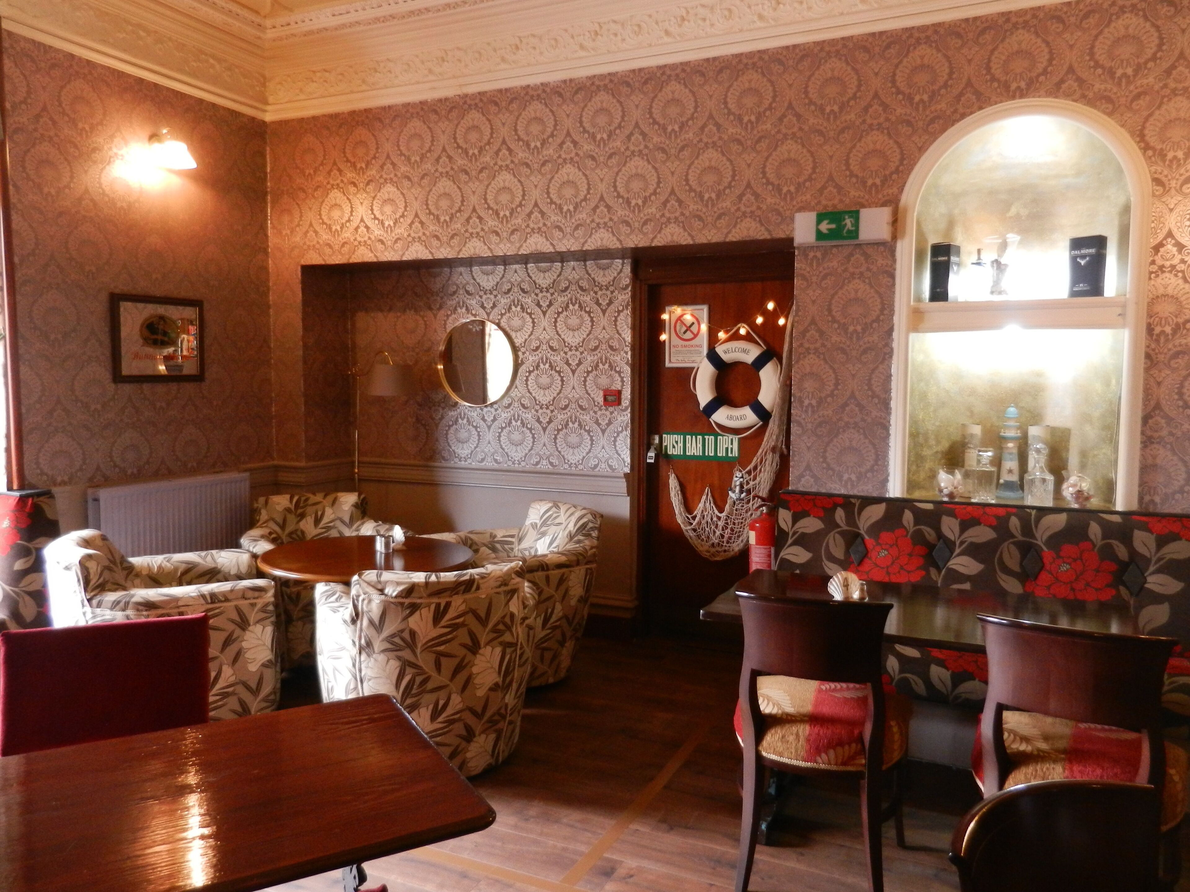 Un interior acogedor con papel tapiz estampado, una zona de bar de madera y diferentes disposiciones de asientos.