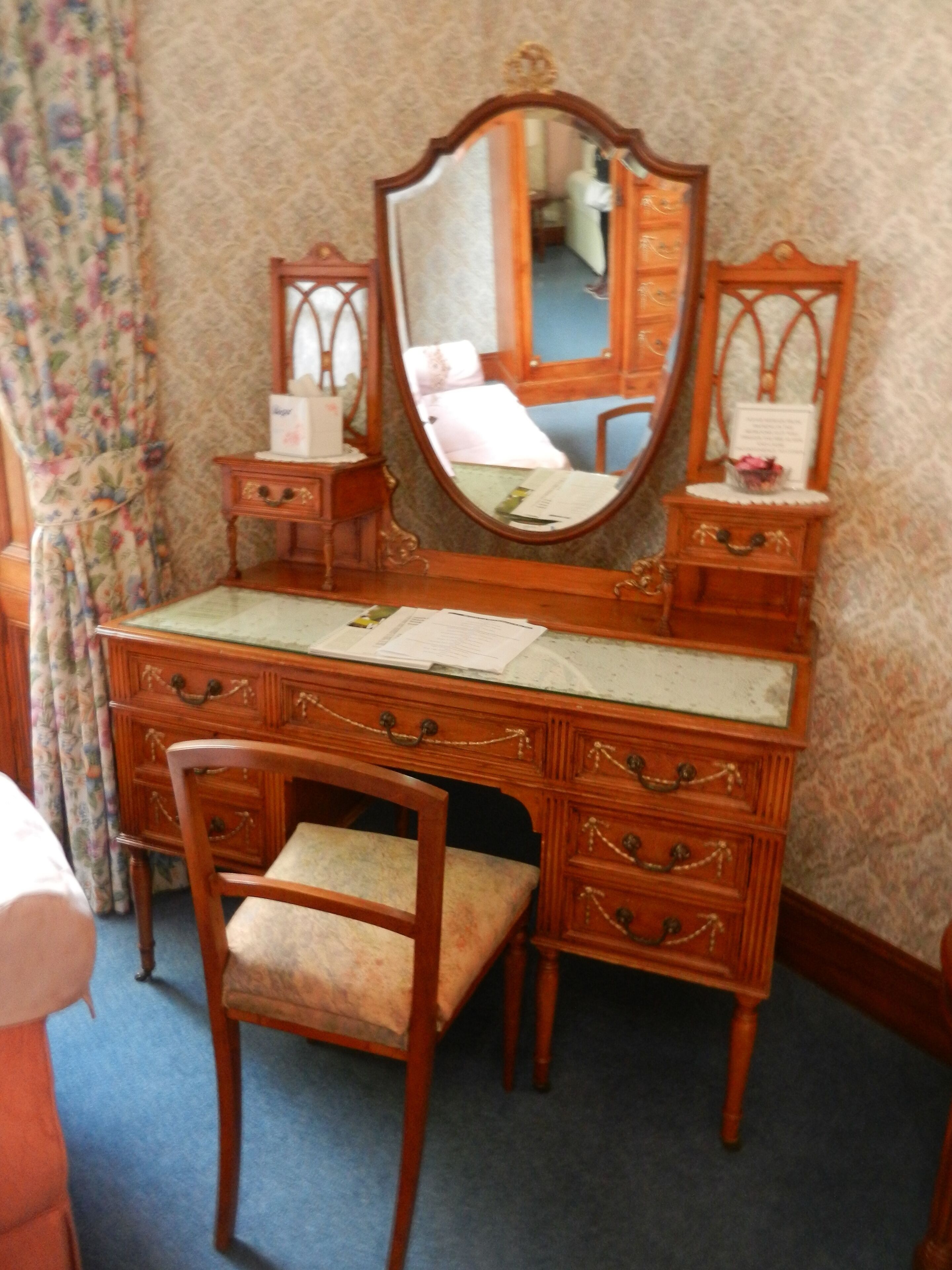 Een houten dressoir met spiegel, een stoel en een tafeltje met zakdoosjes.