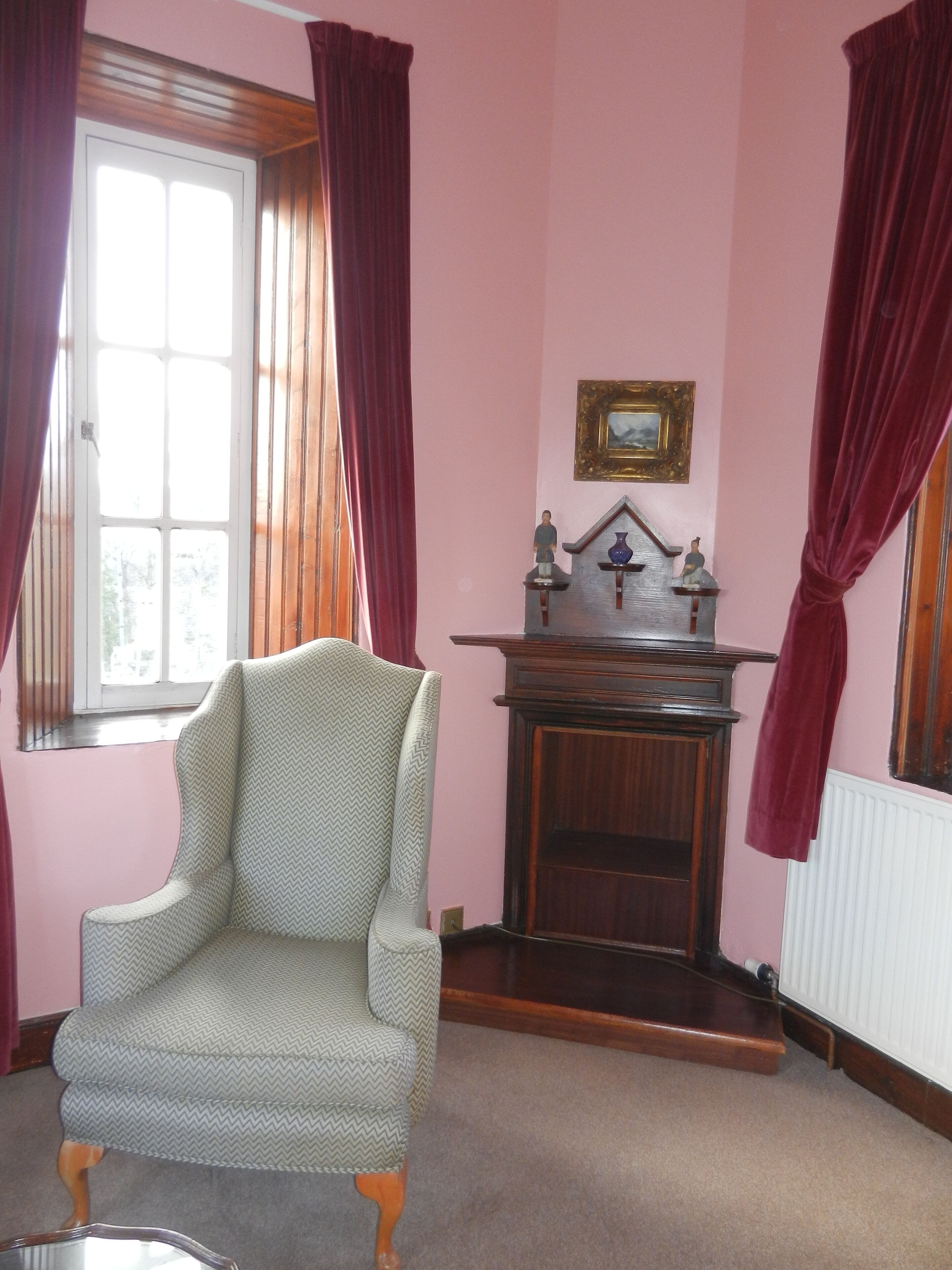 Een kamer met een groot raam, een stoel, een houten kast en een radiator.