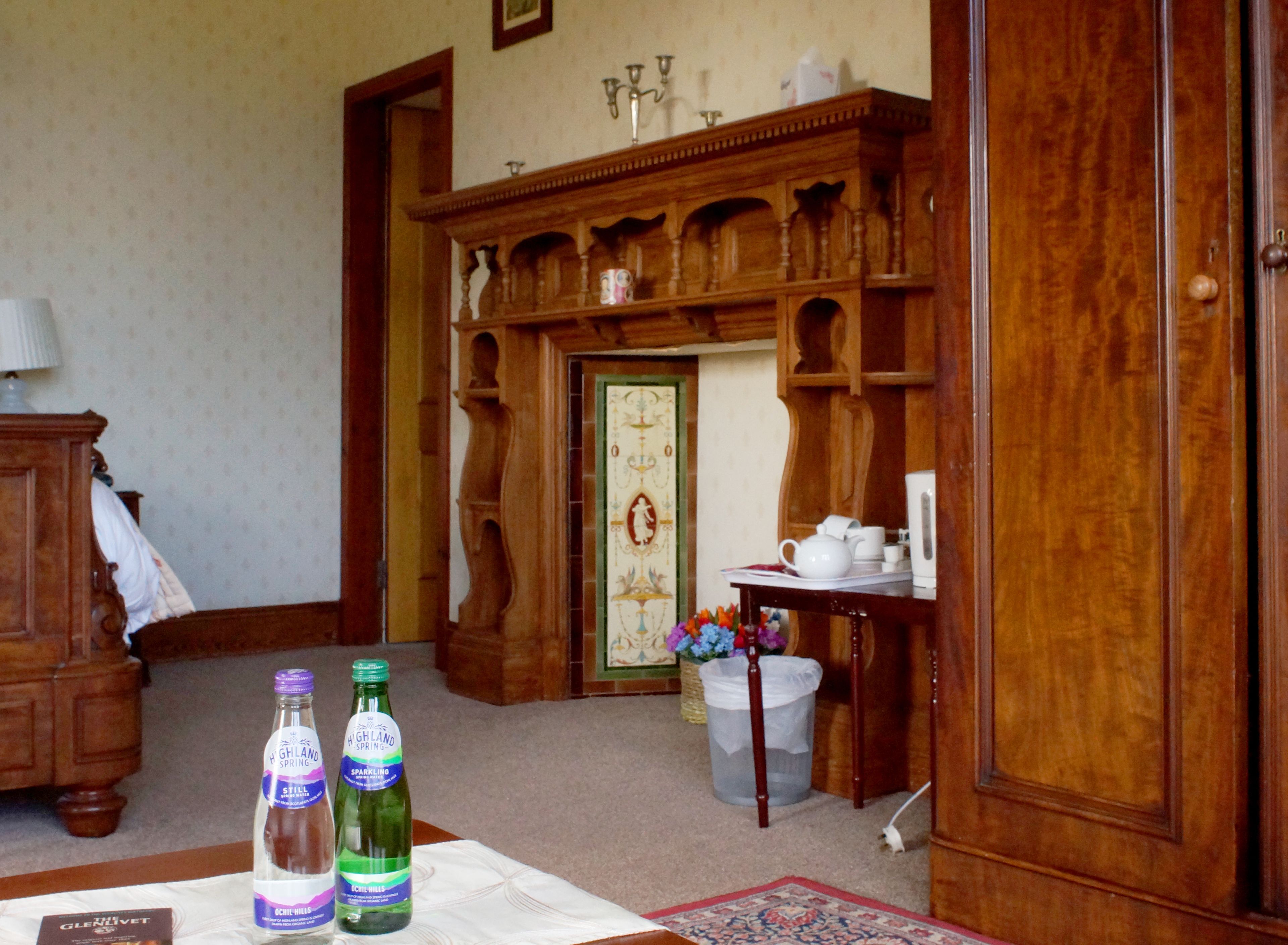 Ein Zimmer mit einem Holzschrank, einem Tisch mit zwei Flaschen sprudelndem Wasser und einem dekorativen Spiegel.