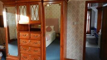 A wooden armoire with glass panels and multiple drawers, a bed with a pink pillow, and a bathroom visible through an open door.