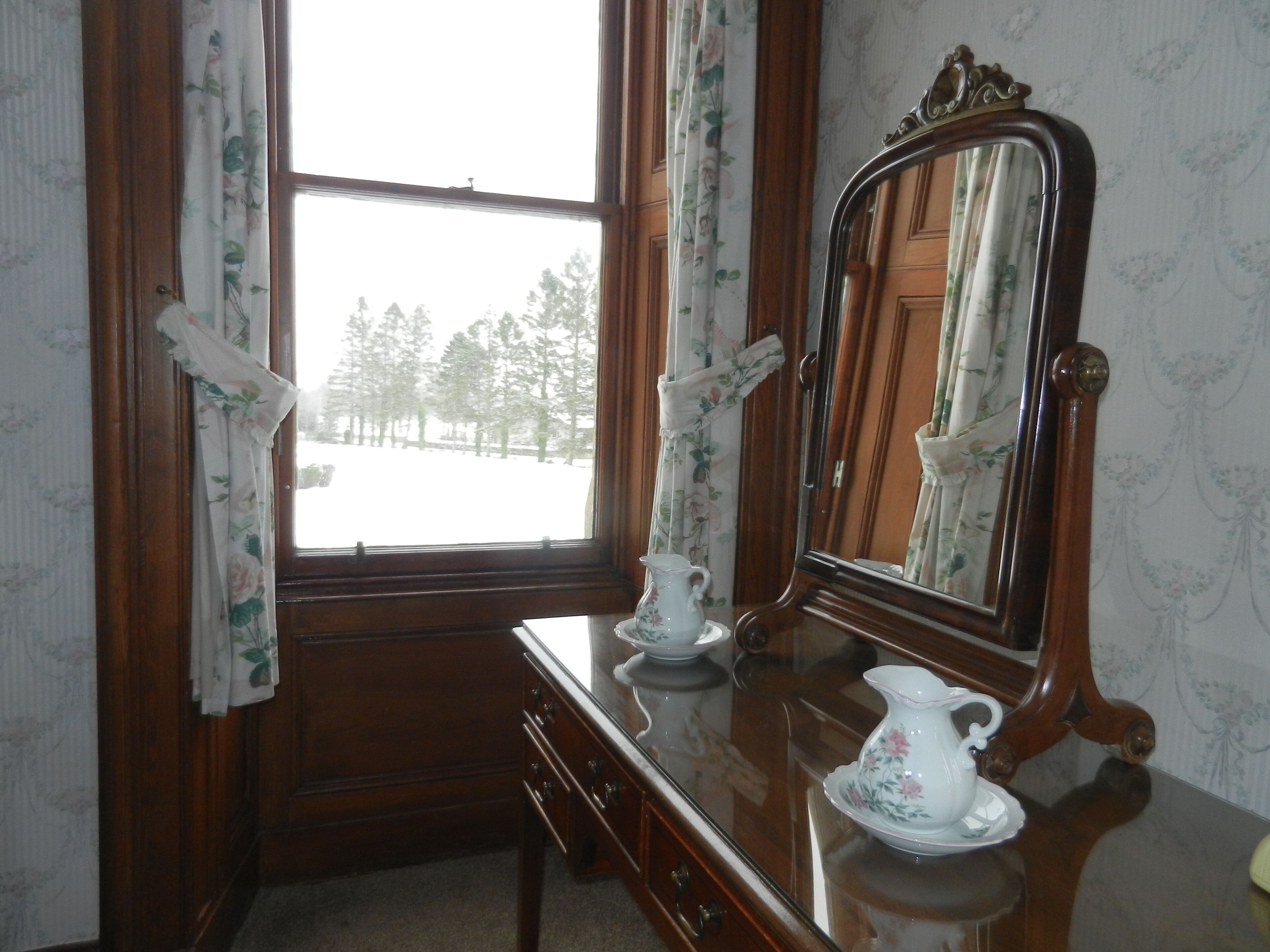 A wooden dresser with a mirror, a pitcher, and a saucer.