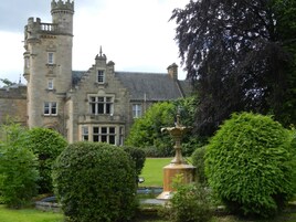A historic stone building with a tower, surrounded by lush greenery and a fountain.