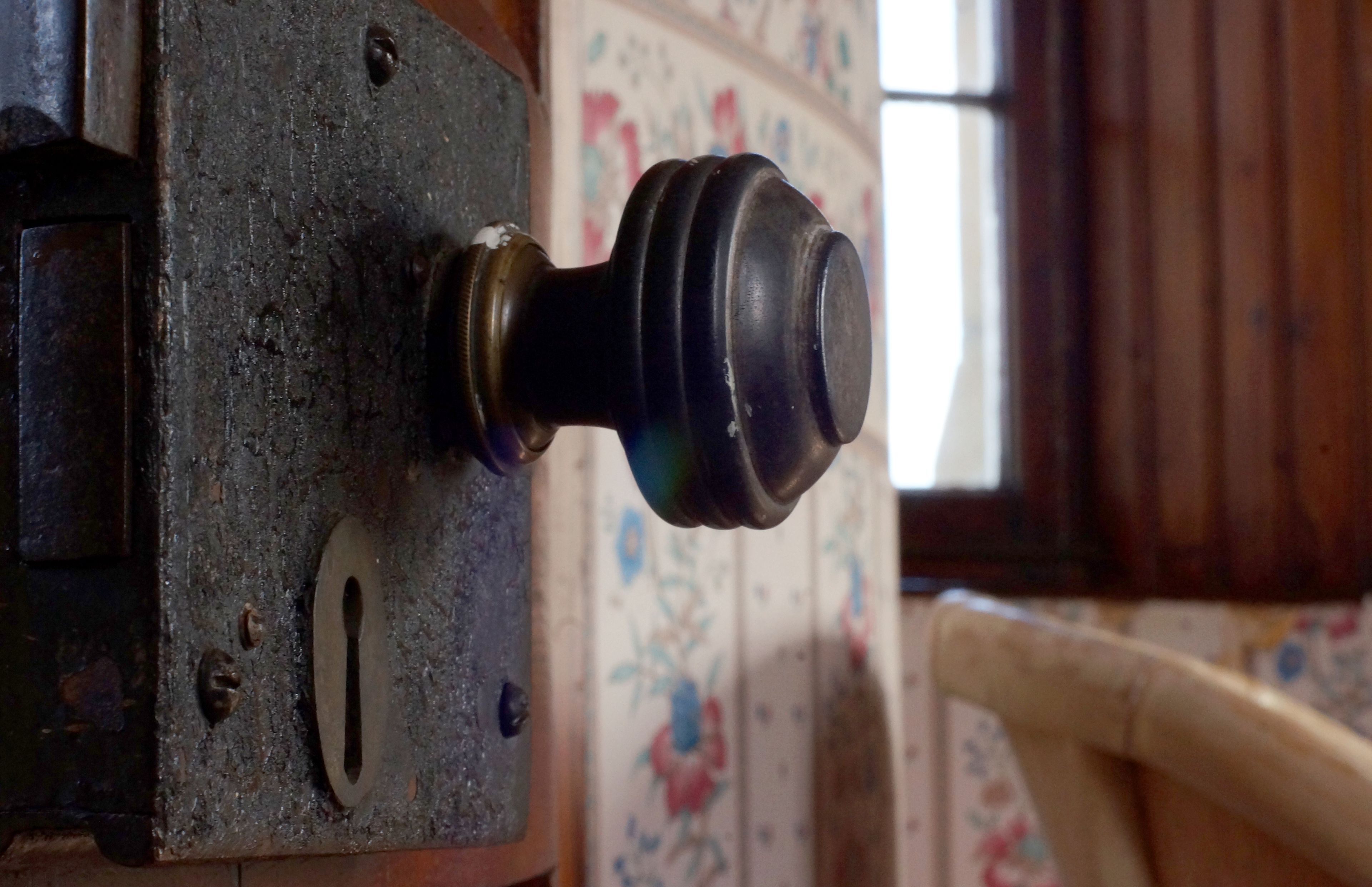 A close-up of a mechanical device with a knob, a metal plate with a hole, and a floral wallpaper pattern in the background.