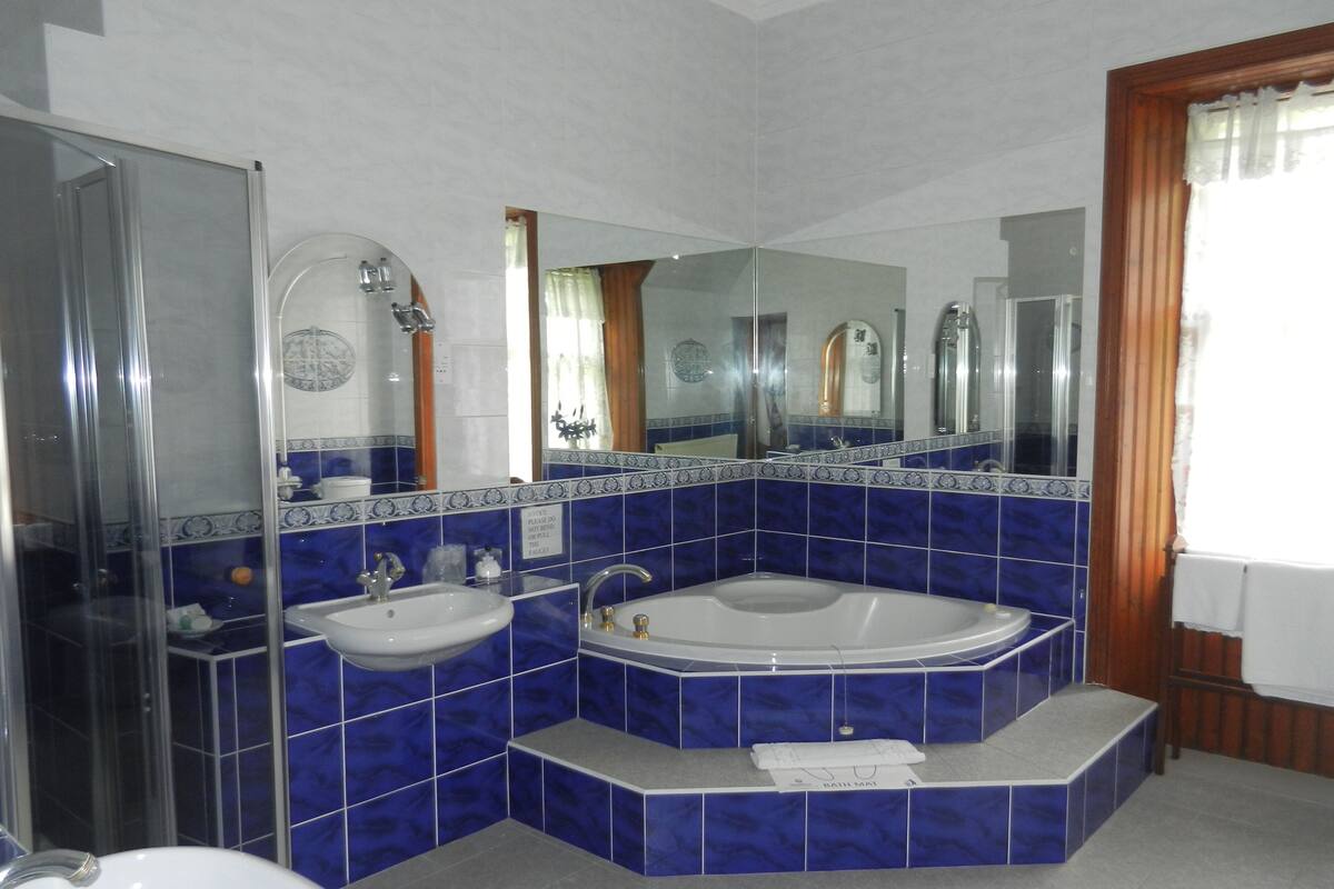 Un baño con ducha, dos lavamanos, bañera y un espejo grande.
