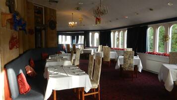 A dining area with tables set for service, a chandelier, and large windows with curtains.