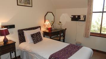 A neatly arranged bedroom with a bed, bedside table, lamp, and a desk with a chair.
