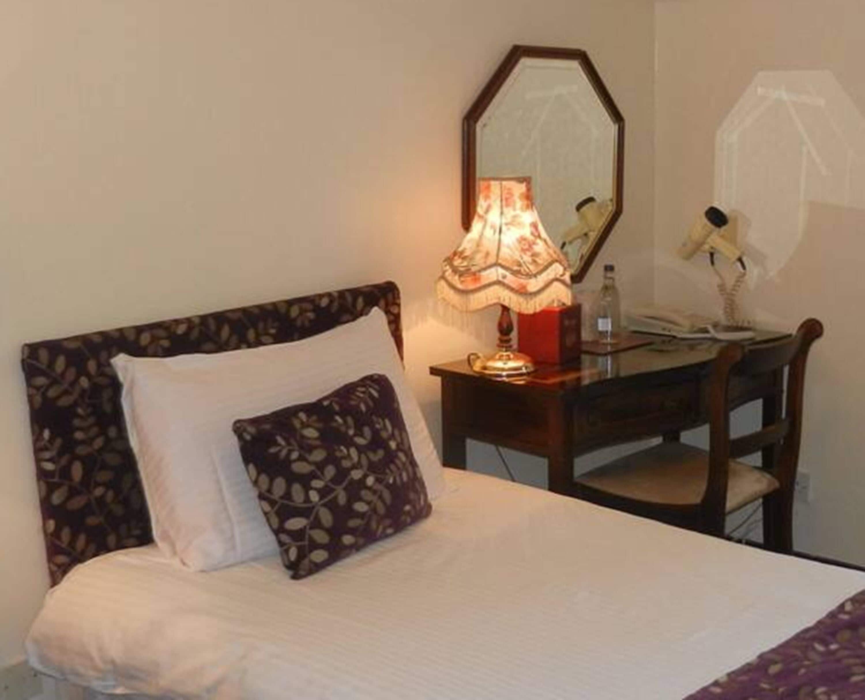 A hotel room with a bed, a nightstand with a lamp, a chair, and a mirror.