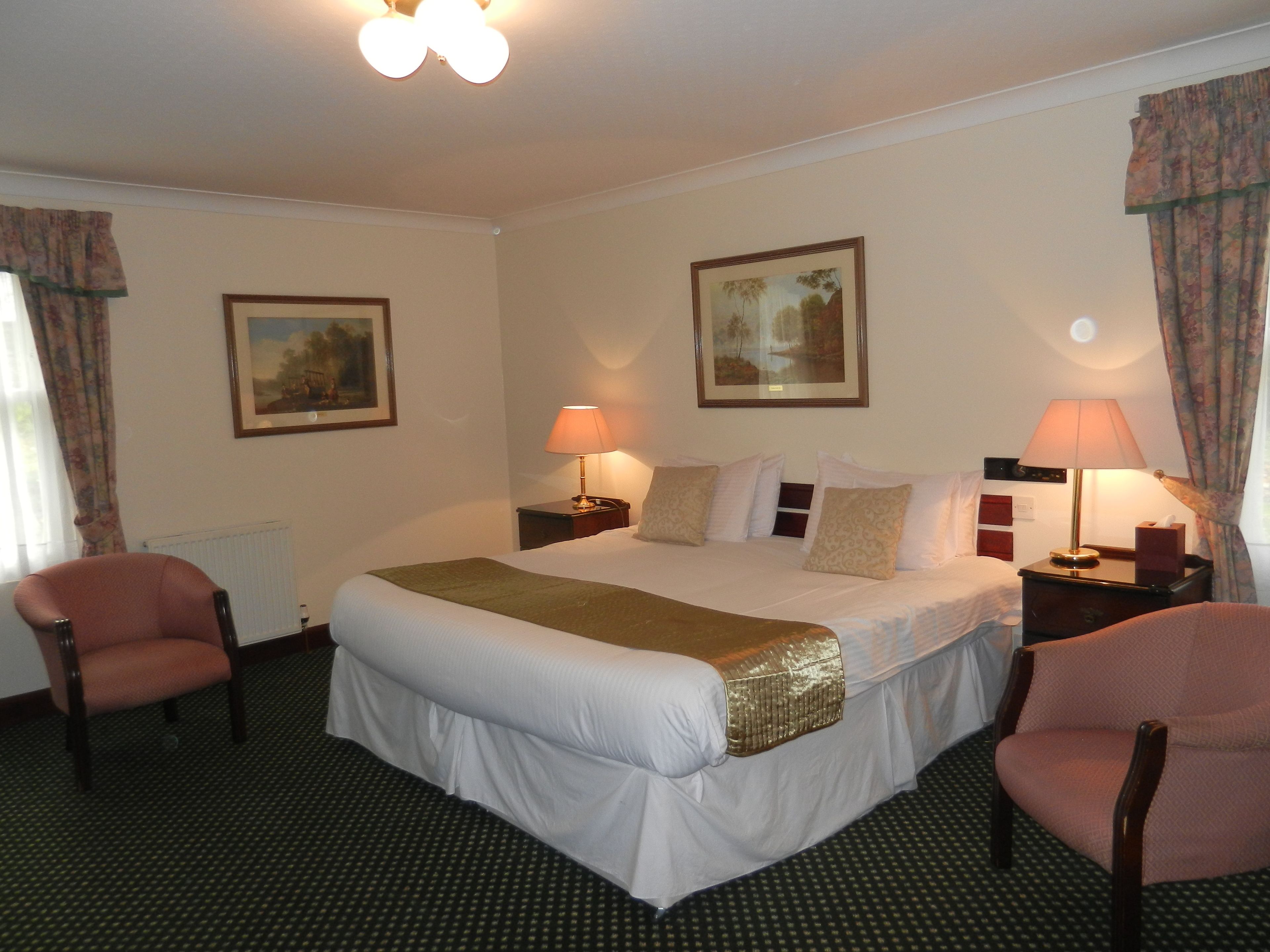 A hotel room with a large bed, two bedside tables, two lamps, two chairs, and two framed pictures on the walls.