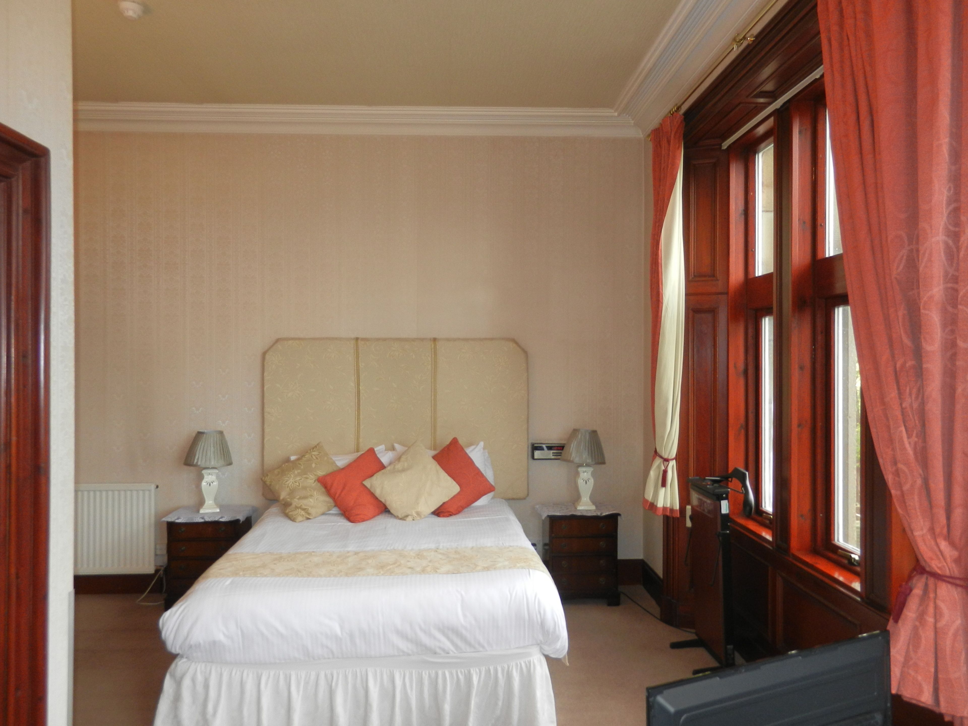 Habitación de hotel con una cama grande, dos mesitas de noche, un radiador y una ventana con cortinas.
