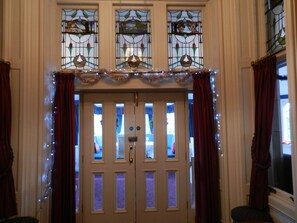 A double door with stained glass windows above, flanked by curtains and string lights. - Morangie Hotel (Tain)
