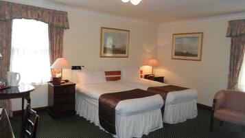 Ein Hotelzimmer mit einem Doppelbett, zwei Nachttischen, einem Sessel, einem Schreibtisch und zwei gerahmten Bildern an den Wänden.