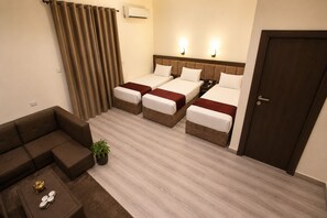 A hotel room with two beds, a sofa, a small table with a plant, and a door.