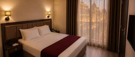 Une chambre d’hôtel avec un grand lit, deux lampes de chevet, un appareil de climatisation, une télévision et une fenêtre avec des rideaux.