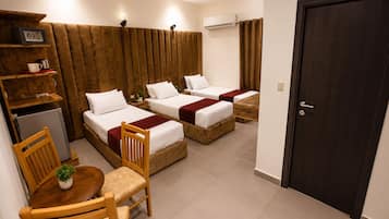Ein Hotelzimmer mit zwei Betten, einem kleinen Tisch mit Stühlen, einer Pflanze, einem Kühlschrank und einer Tür.